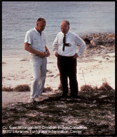 O.J. Noer and another man standing on beach looking at grass